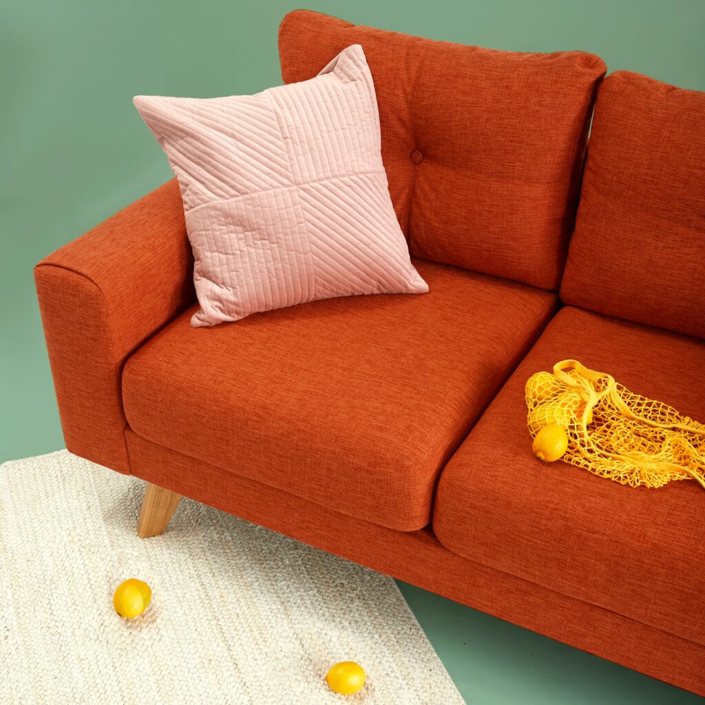 Burnt-orange fabric sofa with a quilted blush cushion against a sage-green wall