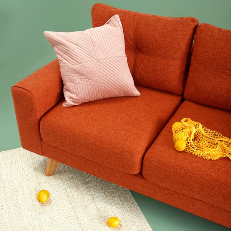 Burnt-orange fabric sofa with a quilted blush cushion against a sage-green wall